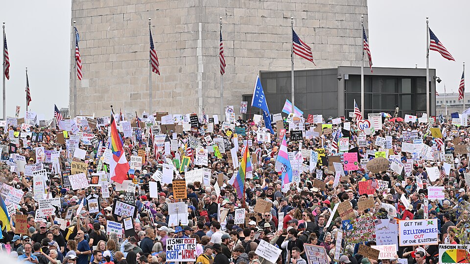 A large crowd of people, many holding signs, in front of the Washington Monument. Hands Off, National Day of Action, Saturday April 5, 2025.  Rally  by the Washington Monument in Washington, DC.