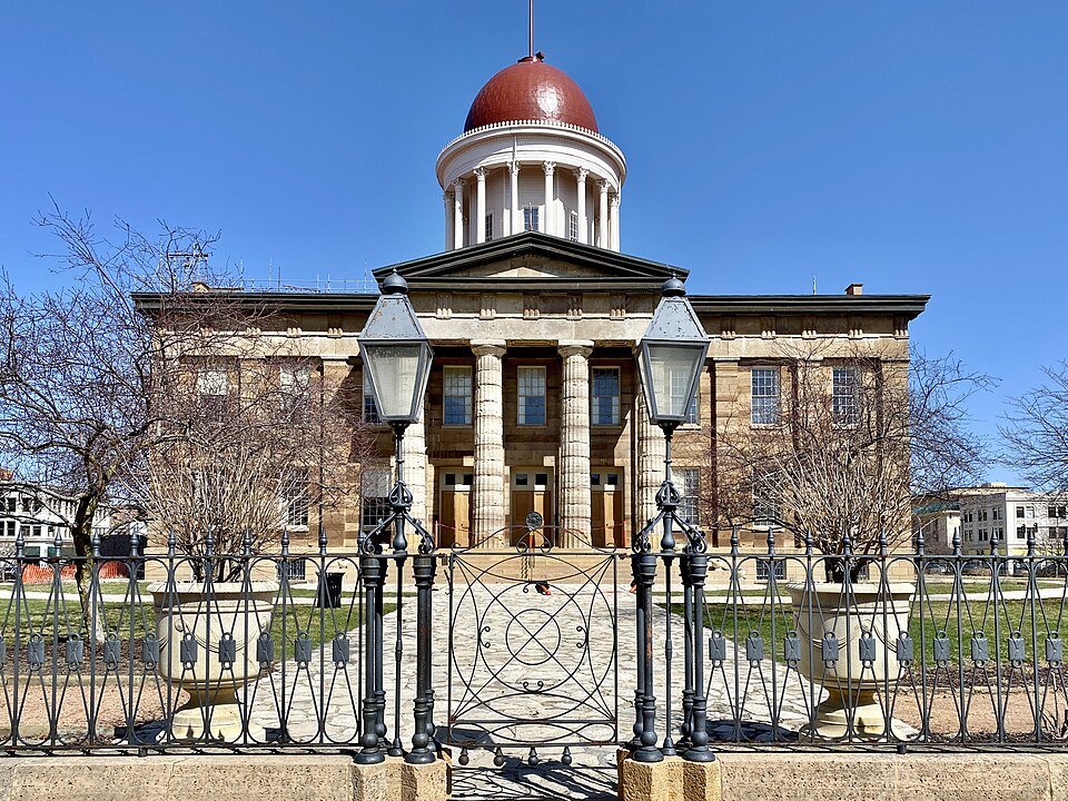 Originally built in 1837-1840, this Greek Revival-style building was designed by John Francis Rague, and constructed to serve as the Illinois State Capitol, replacing the previous state house in Vandalia.  The building features limestone exterior walls, a side-gable roof, two-story doric porticoes o