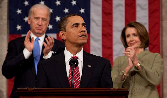 Barack Obama looks on during a joint session of Congress (State of the Union-like) on the night of February 24, 2009.  Standing in front of Vice President Joe Biden and Speaker of the House Nancy Pelosi.