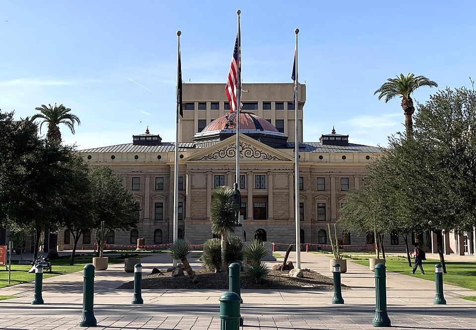 Front view of the Arizona State Capitol building taken at daytime in December 2021, approximately 100 meters away from the entrance. Both the dome and the executive tower are visible.