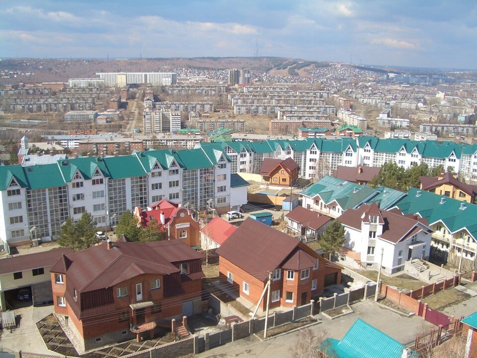 Микрорайон Ершовский
Location: Russia, Irkutsk
Coordinates: 52.2208327, 104.3131684

Caption: This aerial view showcases a sprawling urban landscape under a partly cloudy sky. The foreground features modern, white apartment blocks with distinctive green roofs, alongside smaller, traditional brick ho