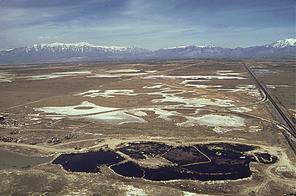 "AERIAL VIEW OF A FIVE ACRE POND NEAR OGDEN, UTAH, THAT CONTAINED ACID WATER, OIL, ACID CLAY SLUDGE, CARS, DEAD ANIMALS AND DUMPED DEBRIS. IT WAS CLEANED UP UNDER EPA'S SUPERVISION TO PREVENT POSSIBLE CONTAMINATION TO A NEARBY WILDLIFE REFUGE AND GREAT SALT LAKE. WHITE AREAS ARE ALKALINE, 04/1974"