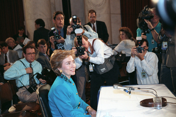 Scope and content:  This item is a photograph of First Lady Hillary Rodham Clinton posing for photographs at a Senate Labor and Human Resources Hearing in the Senate Caucus Room of the Russell Building on Capitol Hill.  The image was photographed by Sharon Farmer.