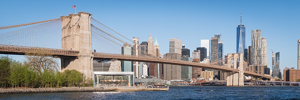 The Brooklyn Bridge and the Lower Manhattan skyline seen from Pebble Beach; the glass pavilion of Jane's Carousel sits below the bridge, with One World Trade Center at right. Brooklyn, New York City.