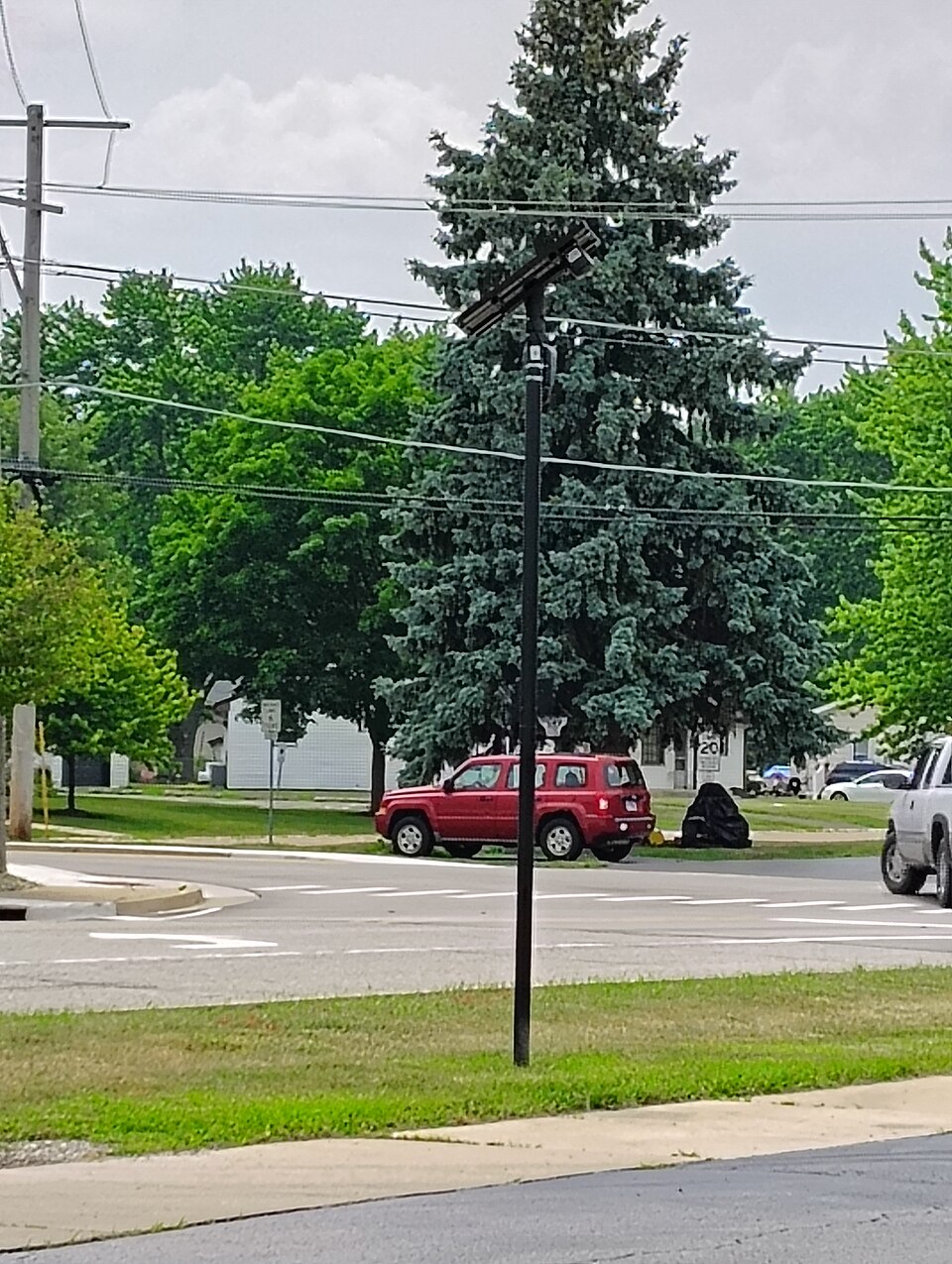 Automatic License Plate Recognition camera, made by Flock Safety, located near the corner of South Main St. and Cross St in Sugar Grove, IL. It consists of a narrow FOV camera mounted to a pole with a solar panel and battery pack. The camera is aimed to capture the license plate numbers and other id