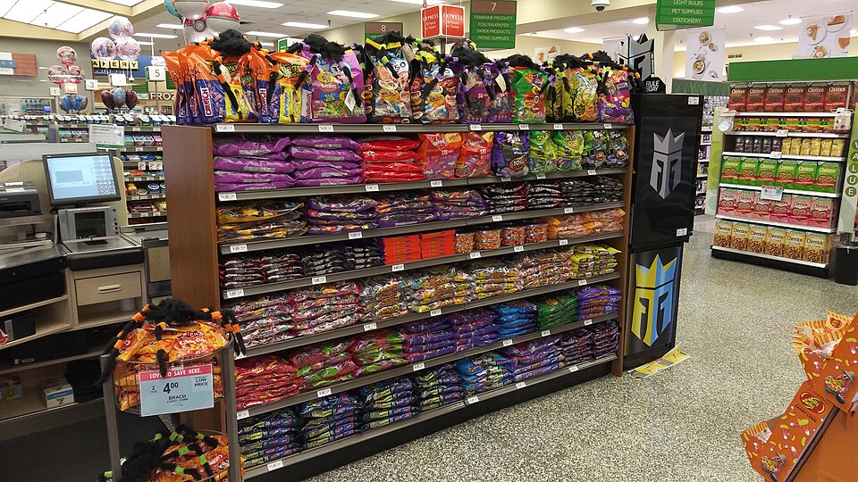 A display of Halloween candy near the checkout lanes in a Publix Super Market in Tri-City Plaza, Clearwater, Florida. On the left side of the image, a cashier station with a computer and register can be seen. Among the candy visible on the shelves and stands of the display are Brach's candy corn, M&