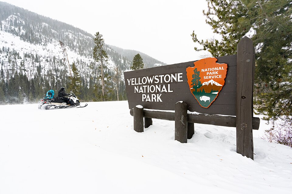 Snowmobiler rides past the Yellowstone National Park East Entrance sign