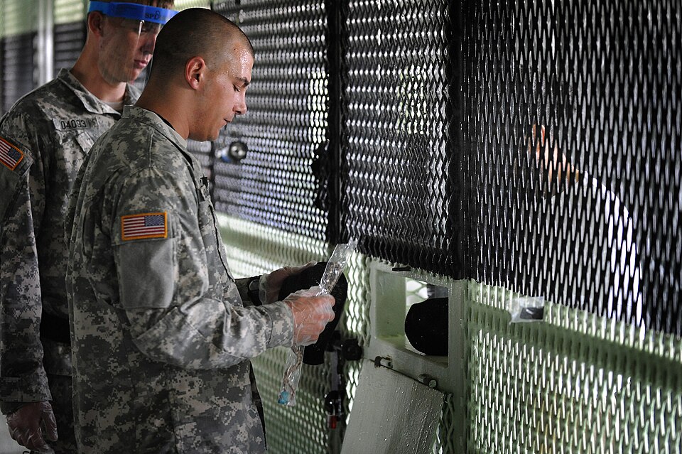 Army Spc. Anthony Berkowitz gives religious items to a detainee in Camp Delta, Joint Task Force Guantanamo, July 7. Berkowitz is a chaplain’s assistant responsible for providing a wide variety of religious items, such as prayer rugs, caps and beads. JTF Guantanamo provides safe, humane, legal and tr