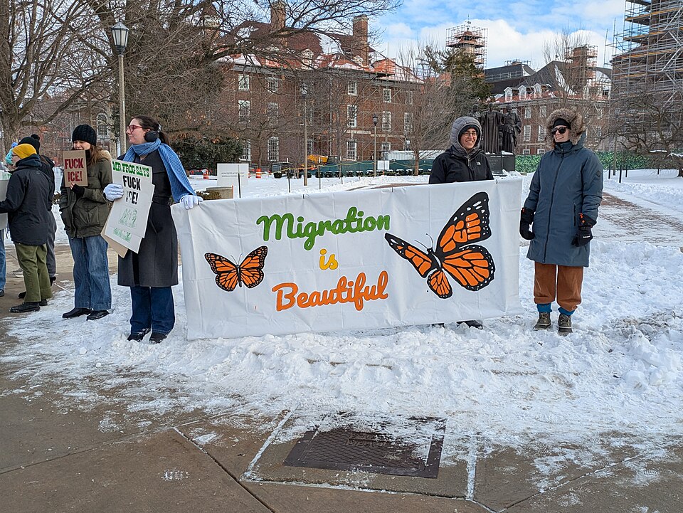 Demonstrators holding a "Migration is Beautiful" sign in front of the Alma Mater