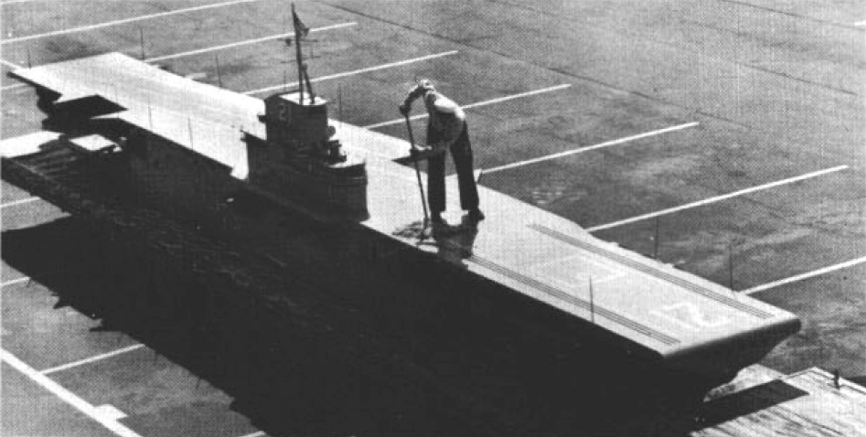 A U.S. Navy sailor swabs the deck of the "USS Quonset Point" for an upcoming display at the Naval Air Station Quonset Point, Rhode Island (USA), circa 1967. The miniature aircraft carrier resembles a SCB-125-modernized Essex-class carrier. However, the pennant number "21" was that of USS Boxer (CV-2