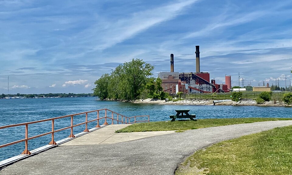 As seen in June 2021: a view looking northwest (downriver) along the Niagara River from Aqua Lane Park in Tonawanda, New York includes the former Charles R. Huntley Generating Station. Installed in 1916 by the Buffalo General Electric Company and at first known as the "River Station", this was a coa