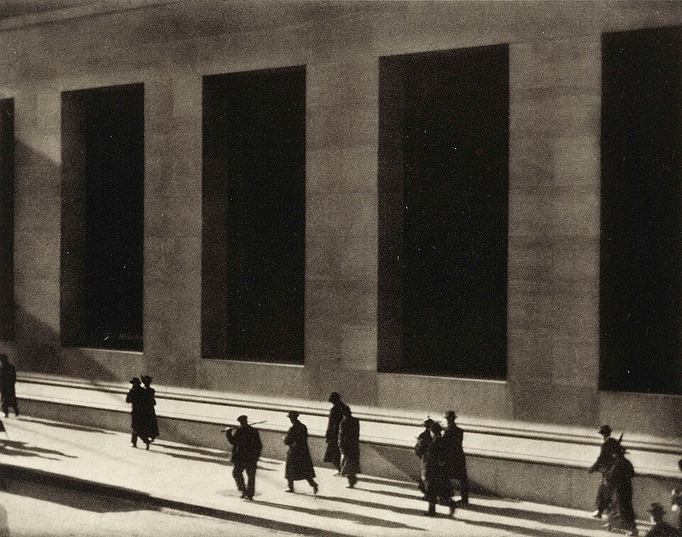Paul Strand took this photograph from the steps of the New York Federal Hall during morning rush hour. The recently completed building of white marble at 23 Wall Street (on the southeast corner of Wall and Broad Streets) was located in one of the most expensive areas of real estate in New York City.