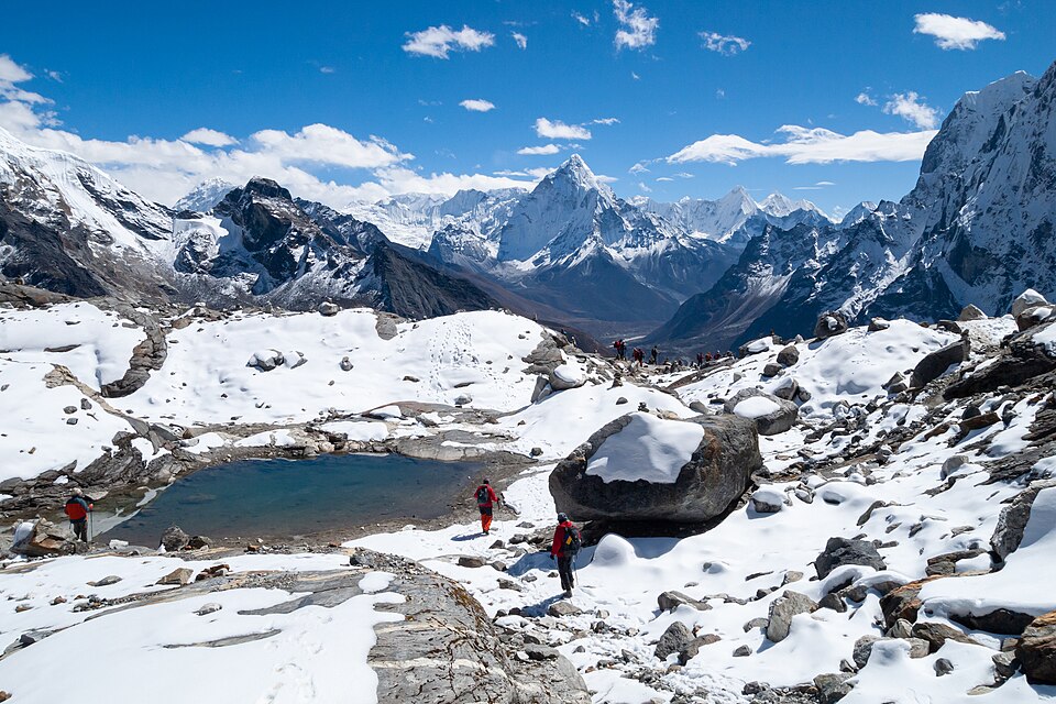 Mountains in snow. Mountain lake. View to the east on descending from Cho La Pass into Chola Valley, 5,200 metres (17,100 ft) a. s. l. Glacial lake, rocks covered with snow, Ama Dablam (6,810 metres (22,343 ft)) and other Himalayan peaks to the south of the Great Himalayan Range in Mahalangur Himal.