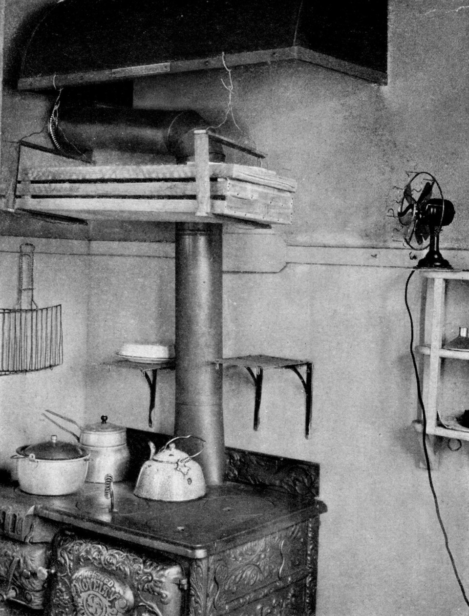THREE LONG, NARROW TRAYS MADE OF FLY SCREEN AND LATHS AND HUNG UP IN A CHEAP SLING OF LATHS AND FENCE WIRE TO THE HOOD OF A KITCHEN STOVE.  It is out of the way of the cook's head and utilizes waste heat, and the vegetables put this distance from the top of the stove do not get too hot.
