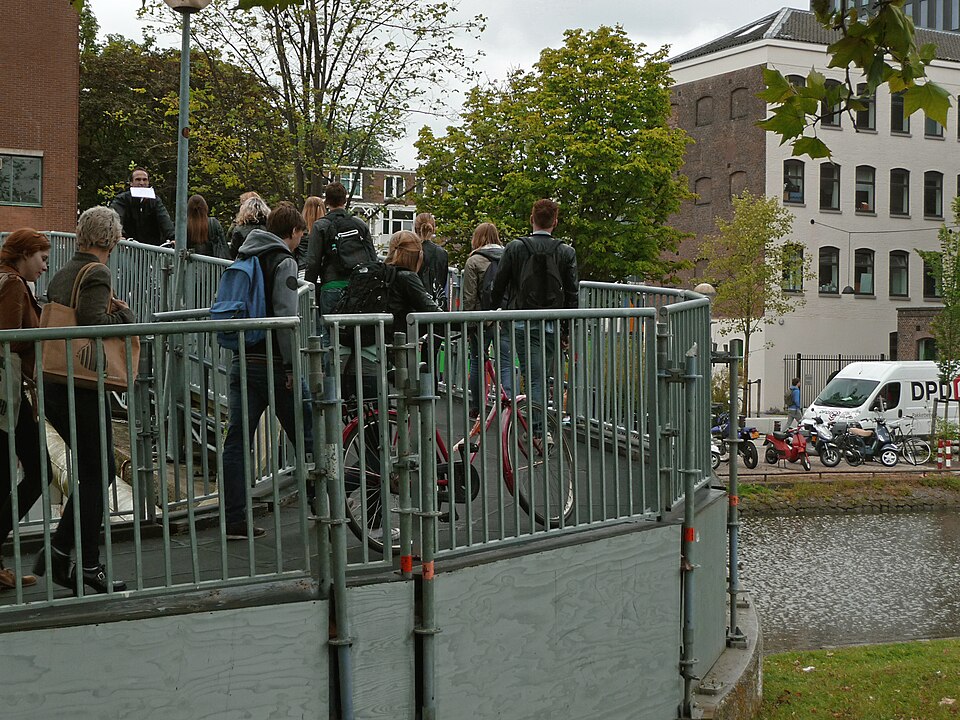 A photo of students walking on the bridge over the canal water Nieuwe Achtergracht, on the university campus Roeterseiland, Amsterdam; free photo in high resolution by Fons Heijnsbroek, June 2013