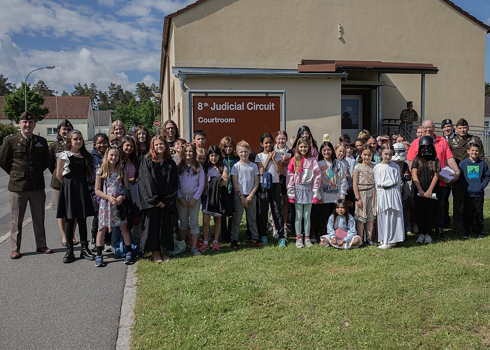 Students attending Grafenwoehr Elementary School pose with Soldiers from 7th Army Training Command Office of the Judge Advocate General before participating in a mock trial in the 8th Judicial Circuit Courtroom at Rose Barracks, Vilseck, Germany, May 20, 2024. This mock trial acted as a practical de